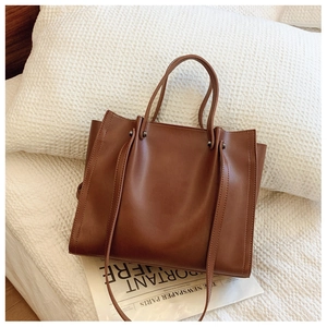 Close-up of deep brown matte leather tote bag with slim handles and metal rivets detail