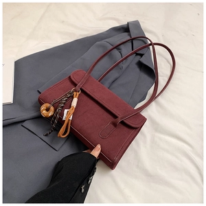 Detail of burgundy frosted leather shoulder bag with decorative charms on grey blazer