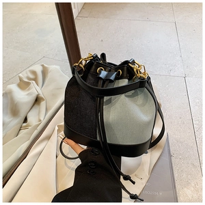Detail of denim bucket bag with gold hardware and drawstring closure on soft background