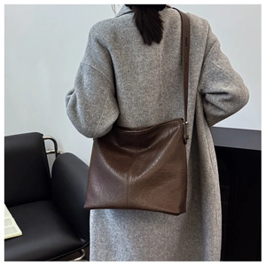Brown vintage leather shoulder bag worn by model with a stylish grey coat in detail