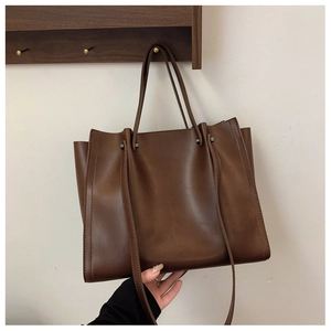Detail of the dark brown matte leather tote bag with side metal rivets and accordion folds