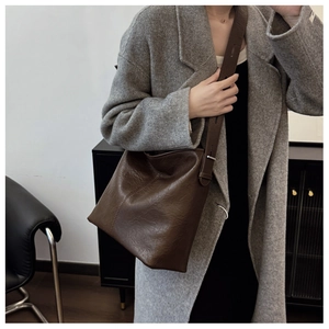 Detail view of large dark brown retro bucket bag with glossy leather texture and wide strap