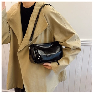 Détail du sac sous le bras en cuir brillant noir avec logo sur un trench-coat kaki