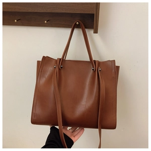Detail of brown tote bag showing side stitching and premium leather texture held by hand