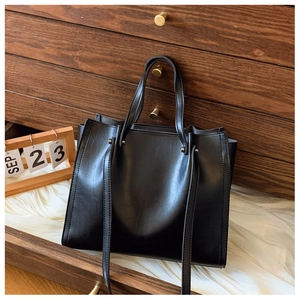 Detail of minimalist black PU tote bag showing leather texture and dual handle system