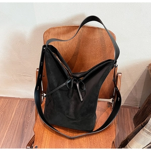 Detail of black suede tote bag with leather strap placed on a vintage wooden chair