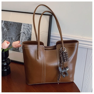 Close-up of brown faux leather tote bag with white contrast stitching and cat charm