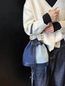 Two-tone denim bucket bag with gold metal handles and drawstring shown on a model