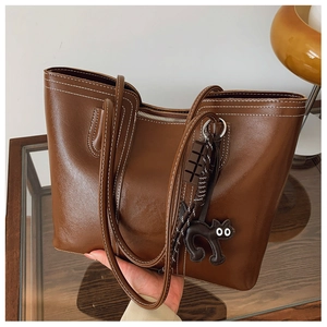 Close-up of brown tote bag featuring white contrast stitching and a cat charm detail