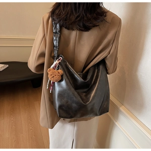 Detail of black PU leather hobo bag featuring a ruffled shoulder strap and plush bear charm
