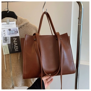 Macro shot of brown leather tote bag showing side stitching and metal hook hardware