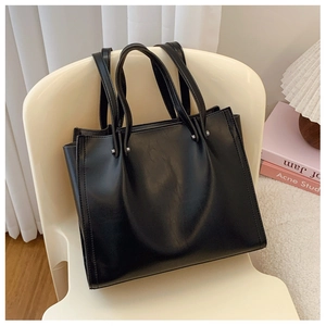 Detail view of large black tote bag showing gusseted sides and slim shoulder straps