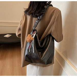 Detail of black leather tote bag featuring a trendy scrunchie strap and cute bear charm