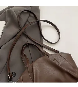 Detail of adjustable slim shoulder strap and silver metal hardware on brown PU bag