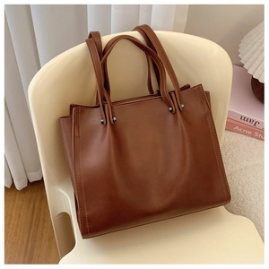 Detailed view of deep brown leather tote bag with sturdy handles on a stylish chair