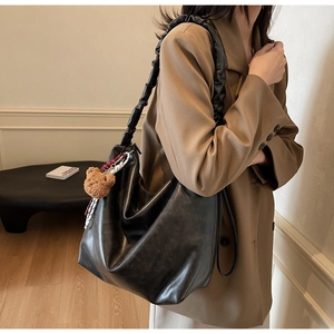Close-up of black hobo bag with scrunchie strap, bear charm and striped scarf detail