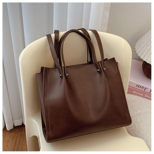 Close-up of a dark brown matte leather tote bag with dual straps and silver rivet details
