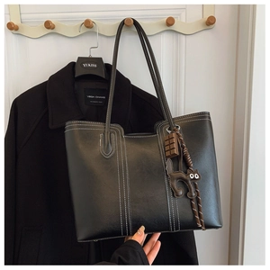 Detail of black tote bag with white contrast stitching and cute cat bag charm