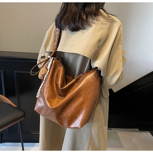 Brown leather bucket bag detail with plush charm and woven strap on model side view