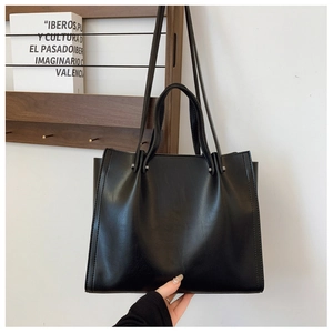 Detail of a black minimalist tote bag with smooth PU leather texture and dual handle straps