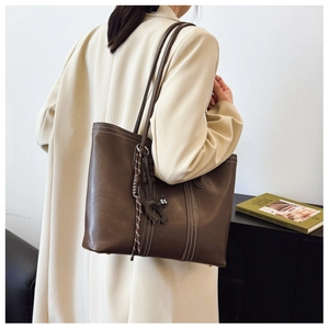 Detail of dark brown tote bag with white contrast stitching and a cat pendant charm