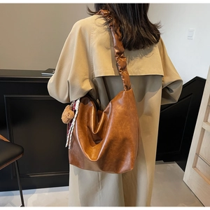 Detail of a large brown faux leather bucket bag featuring a unique ruched shoulder strap