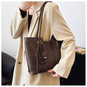 Detail of dark brown tote bag with white stitching and cute cat charm on beige blazer