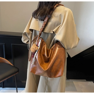 Close-up of caramel leather tote bag featuring cloud pleated strap and teddy bear charm