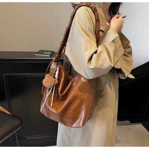 Detail view of brown PU leather hobo bag with thick pleated strap and cute bear charm