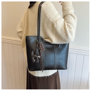 Detail of black leather tote bag with white contrast stitching and cat pendant