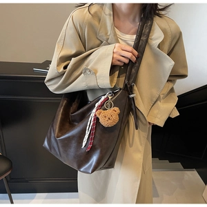Detail of dark brown leather tote bag with plush bear charm and striped woven strap