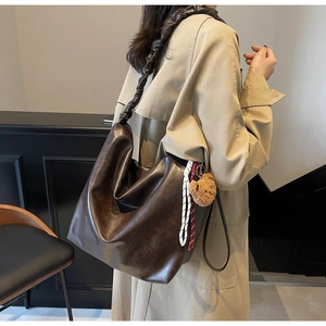 Detail of dark brown leather tote bag with unique ruched strap and cute bear charm