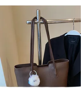 Detailed view of brown leather tote bag handle with soft white plush ball charm accessory