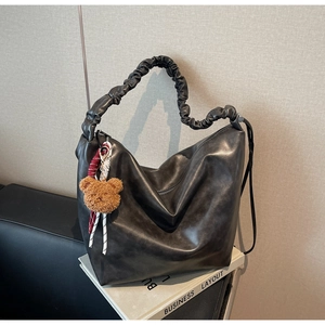 Detail of a black bucket bag with ruffled handle and a brown plush bear charm accessory