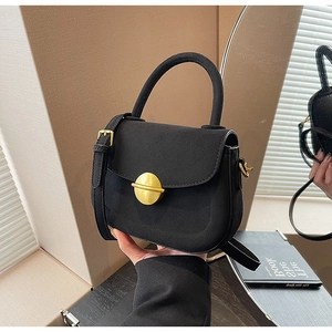 Close-up of black suede saddle bag featuring a distinctive round gold metal buckle