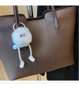 Detail of a large brown tote bag featuring a cute white fluffy charm on the strap