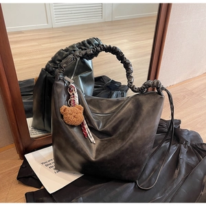 Detail of black glossy faux leather tote bag with pleated handle and plush bear charm