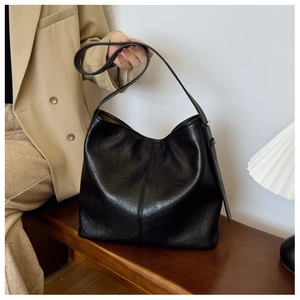 Minimalist black faux leather hobo bag on a wooden bench with textured finish