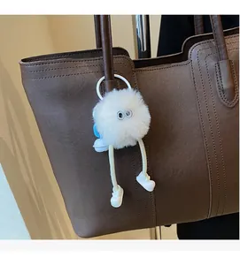 Detail of a white fluffy plush doll charm with big eyes on a brown leather tote bag