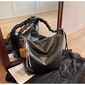 Detail of black leather bucket bag with pleated shoulder strap and brown bear charm