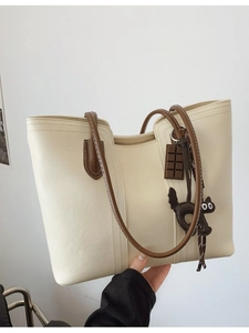 Minimalist beige leather tote bag with brown straps and cute black cat charm accessory