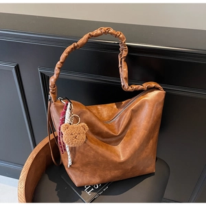 Detailed view of the brown leather tote bag featuring a ruched shoulder strap and bear charm