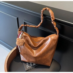 Detail of caramel brown hobo bag featuring pleated shoulder strap and teddy bear charm