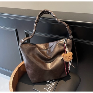 Close-up of deep brown leather bucket bag with unique pleated strap and cute bear charm