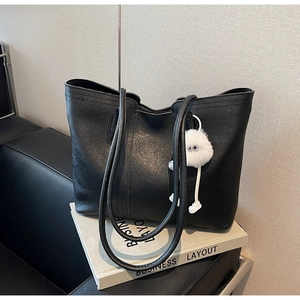 Detail of black leather tote bag with monster charm on a minimalist sofa