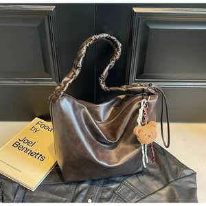 Detail of hobo bag with pleated handle, plush bear charm and soft brown leather texture