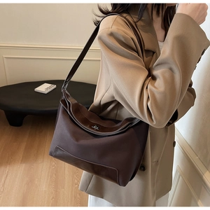 Detailed side view of a vintage dark brown shoulder bag worn by a model in a blazer