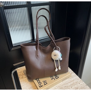 Detail of a large coffee brown tote bag with a white plush monster charm on a stone surface