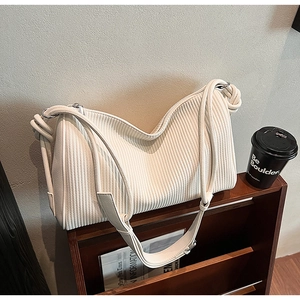 Detail of cream shoulder bag with vertical stripe texture and knotted strap on wooden stand