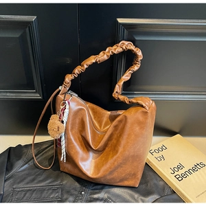 Detail of a brown leather shoulder bag featuring a pleated cloud strap and a bear charm